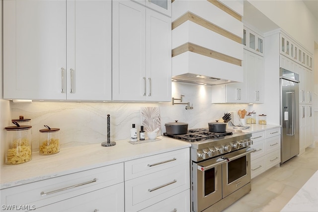 kitchen featuring premium range hood, high quality appliances, white cabinetry, decorative backsplash, and light stone countertops