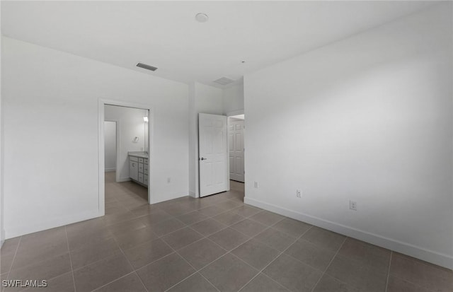 unfurnished bedroom with baseboards, visible vents, connected bathroom, and dark tile patterned flooring