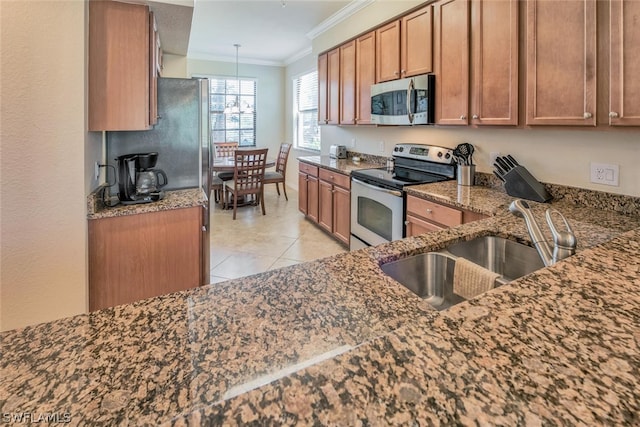 kitchen featuring crown molding, stainless steel appliances, brown cabinetry, a sink, and dark stone countertops