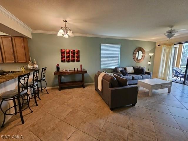 living room with ceiling fan with notable chandelier, crown molding, baseboards, and light tile patterned floors