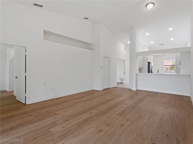 unfurnished living room featuring recessed lighting, visible vents, high vaulted ceiling, light wood-type flooring, and baseboards