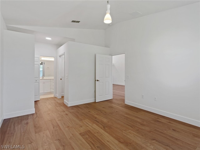 unfurnished bedroom featuring light wood-type flooring, visible vents, lofted ceiling, and baseboards