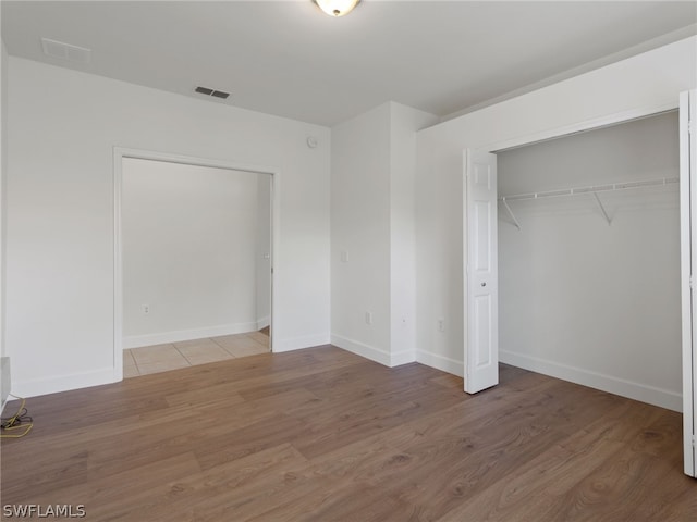 unfurnished bedroom with baseboards, a closet, visible vents, and wood finished floors