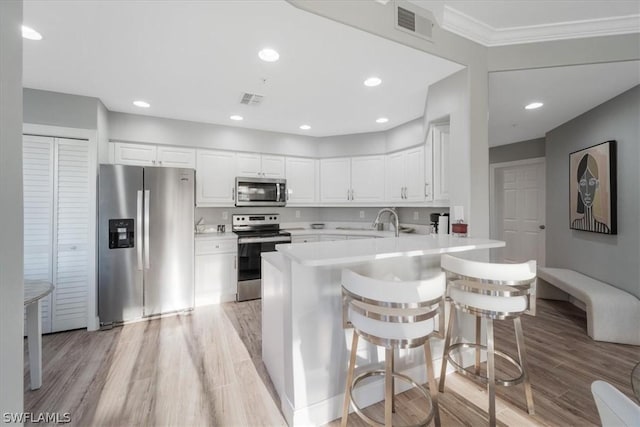 kitchen with white cabinets, a kitchen bar, stainless steel appliances, light hardwood / wood-style floors, and kitchen peninsula