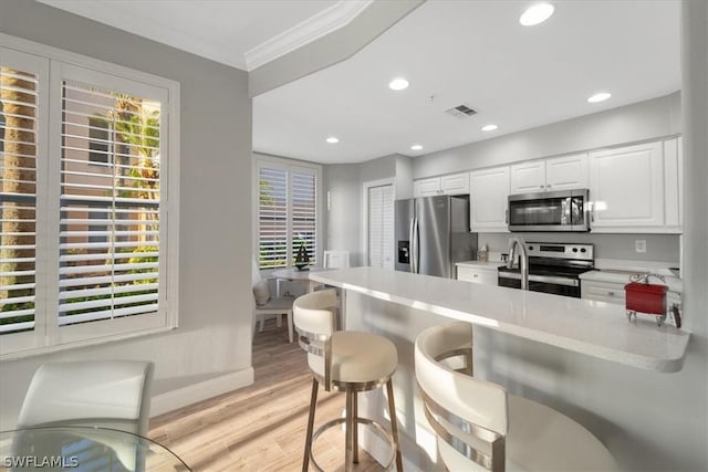 kitchen featuring white cabinetry, stainless steel appliances, a breakfast bar, light hardwood / wood-style flooring, and crown molding