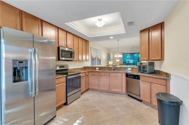 kitchen with kitchen peninsula, appliances with stainless steel finishes, pendant lighting, a raised ceiling, and sink