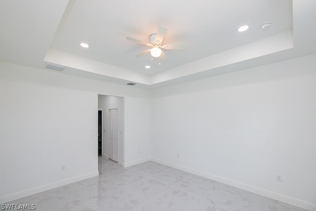 tiled empty room with ceiling fan and a tray ceiling