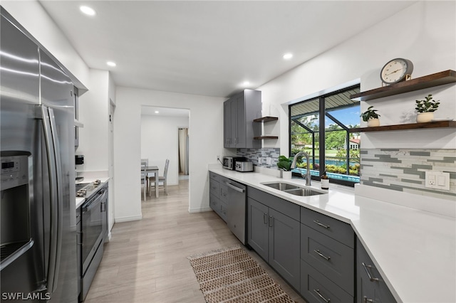 kitchen with appliances with stainless steel finishes, light hardwood / wood-style flooring, tasteful backsplash, sink, and gray cabinets