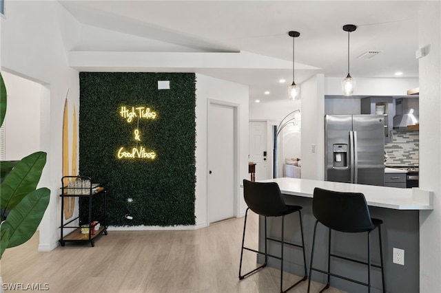 kitchen with a kitchen bar, appliances with stainless steel finishes, tasteful backsplash, wall chimney range hood, and light wood-type flooring