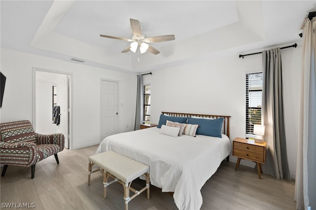 bedroom with multiple windows, light wood-type flooring, and a tray ceiling