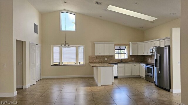 kitchen with a skylight, decorative backsplash, high vaulted ceiling, and stainless steel appliances