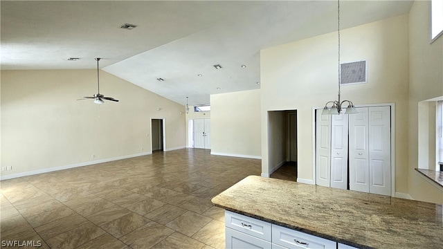 interior space with white cabinets, tile patterned flooring, ceiling fan with notable chandelier, dark stone countertops, and high vaulted ceiling