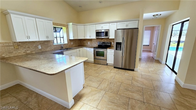 kitchen with appliances with stainless steel finishes, kitchen peninsula, white cabinets, and backsplash