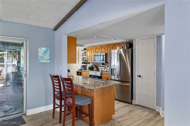 kitchen featuring dark stone counters, stainless steel appliances, light wood-type flooring, and kitchen peninsula