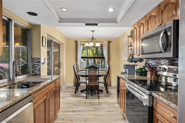 kitchen featuring light hardwood / wood-style flooring, stainless steel appliances, sink, backsplash, and a tray ceiling