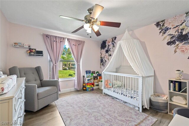 bedroom with a crib, light wood-type flooring, and ceiling fan