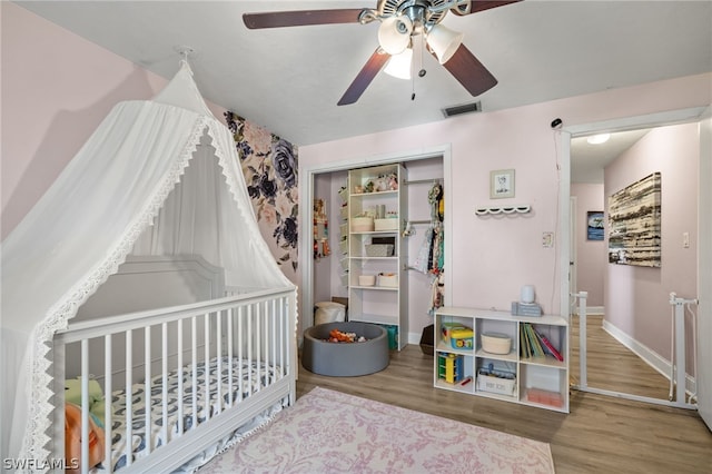 bedroom with a crib, ceiling fan, hardwood / wood-style flooring, and a closet