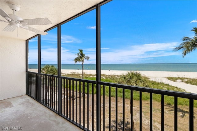 unfurnished sunroom with a water view, a view of the beach, and ceiling fan