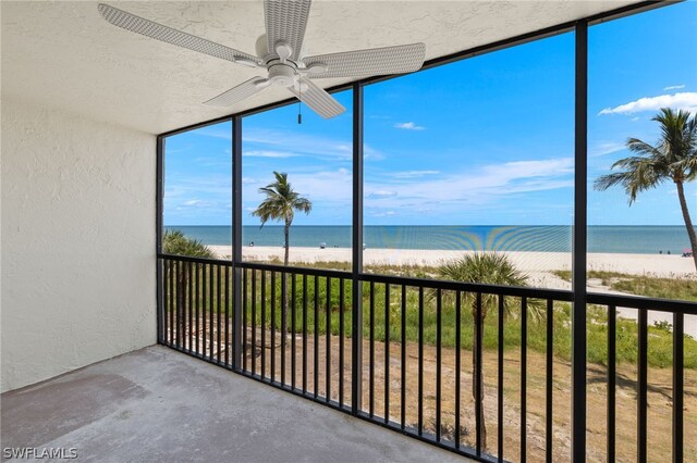 unfurnished sunroom featuring a water view, a view of the beach, and ceiling fan