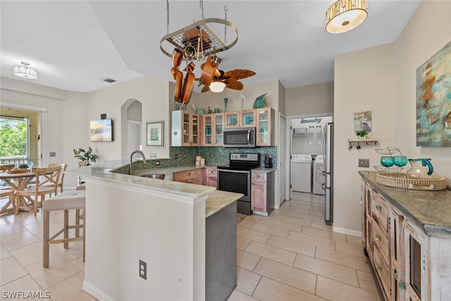 kitchen with tasteful backsplash, kitchen peninsula, appliances with stainless steel finishes, light tile patterned floors, and independent washer and dryer