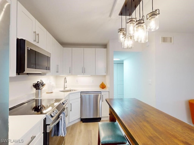 kitchen with stainless steel appliances, sink, hanging light fixtures, light hardwood / wood-style floors, and white cabinetry