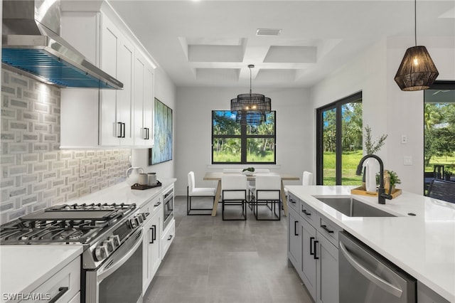 kitchen with appliances with stainless steel finishes, decorative backsplash, tile patterned floors, wall chimney exhaust hood, and coffered ceiling