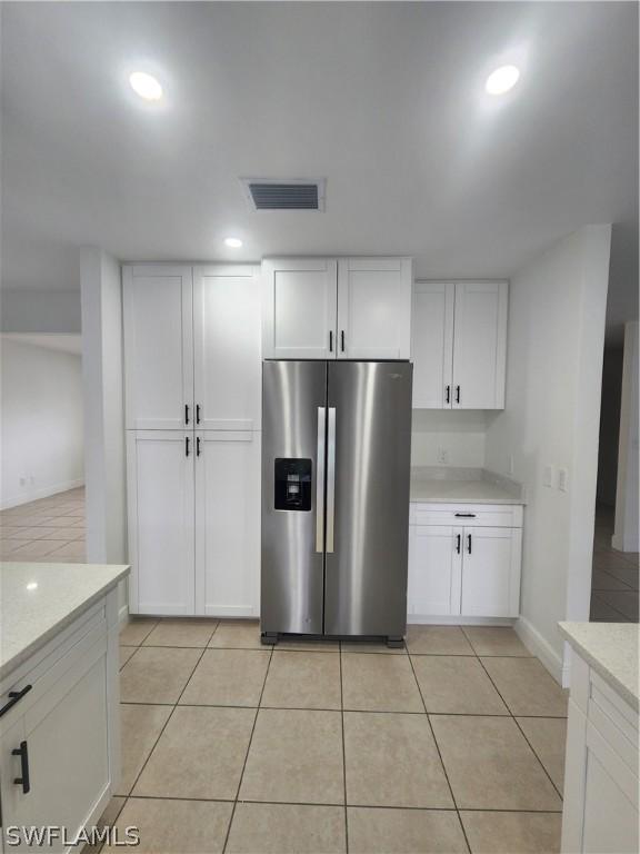 kitchen featuring white cabinetry, light tile patterned floors, light stone countertops, and stainless steel refrigerator with ice dispenser