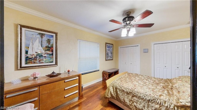 bedroom with two closets, hardwood / wood-style flooring, crown molding, and ceiling fan