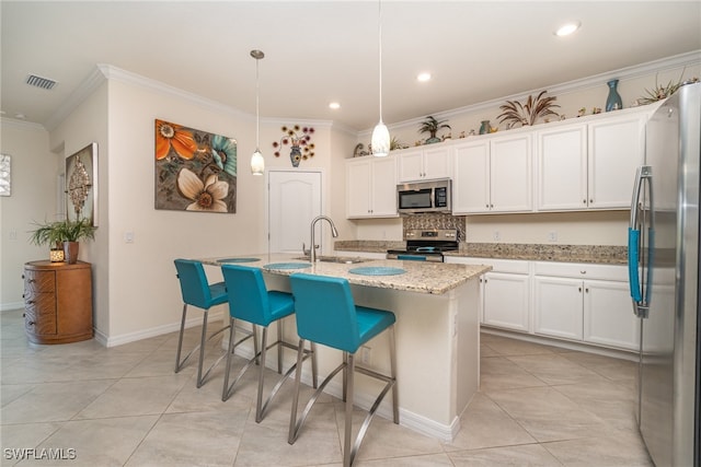 kitchen featuring light stone countertops, an island with sink, stainless steel appliances, and decorative light fixtures