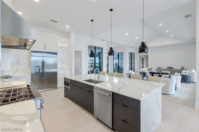 kitchen with white cabinetry, built in appliances, wall chimney exhaust hood, sink, and light stone counters