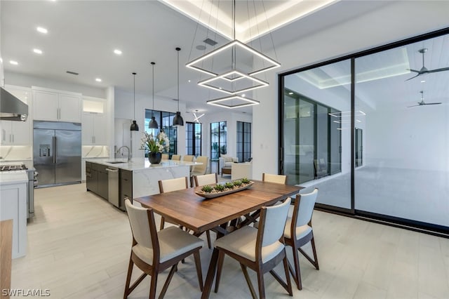 dining area with ceiling fan with notable chandelier, sink, and light wood-type flooring