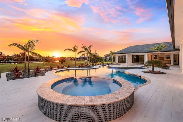 pool at dusk featuring an in ground hot tub and a patio