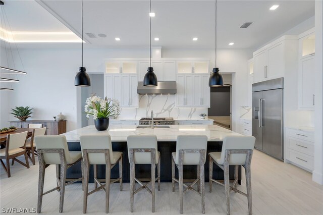 kitchen with decorative light fixtures, built in refrigerator, and wall chimney range hood