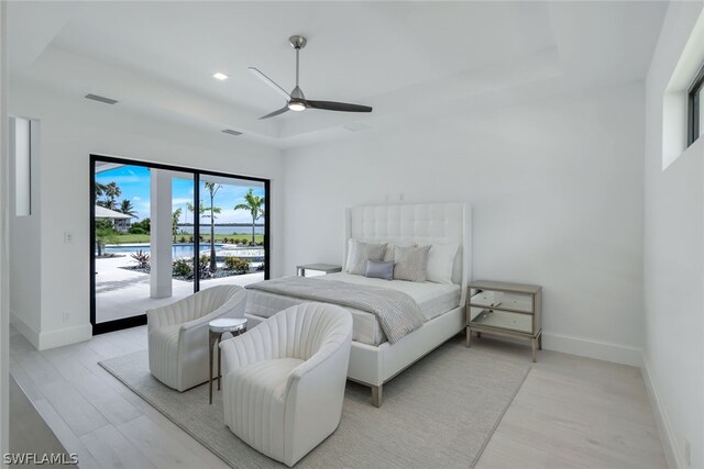 bedroom with light hardwood / wood-style floors, access to outside, a raised ceiling, and ceiling fan