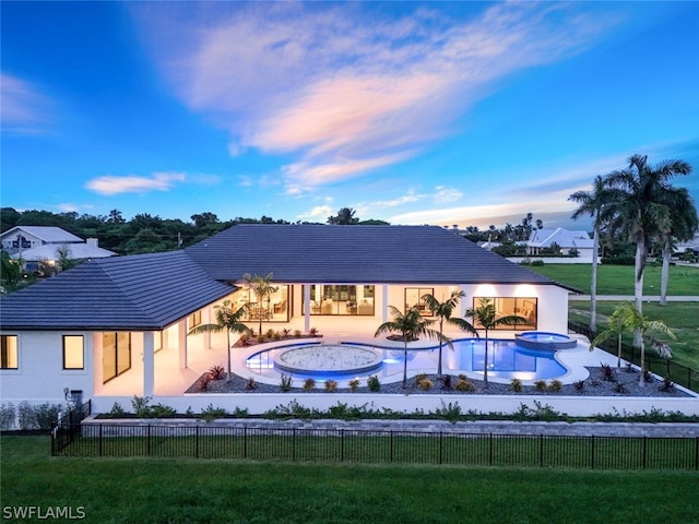 back house at dusk with a lawn and a fenced in pool