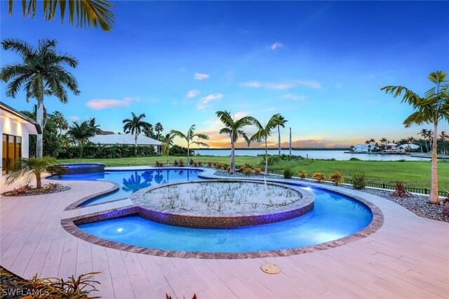 pool at dusk with an in ground hot tub and a water view