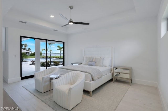 bedroom with access to exterior, ceiling fan, a raised ceiling, a water view, and light hardwood / wood-style flooring