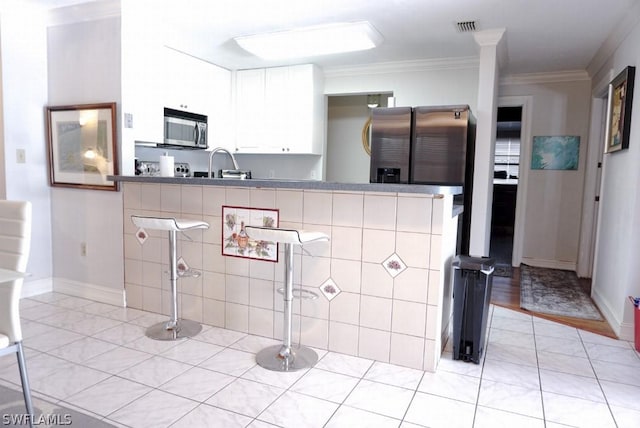 kitchen featuring a peninsula, stainless steel appliances, visible vents, white cabinets, and a kitchen bar