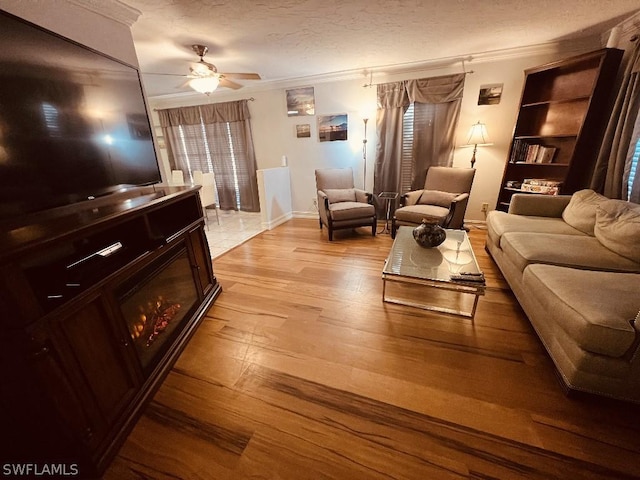 living area with light wood-style floors, ornamental molding, ceiling fan, a textured ceiling, and baseboards