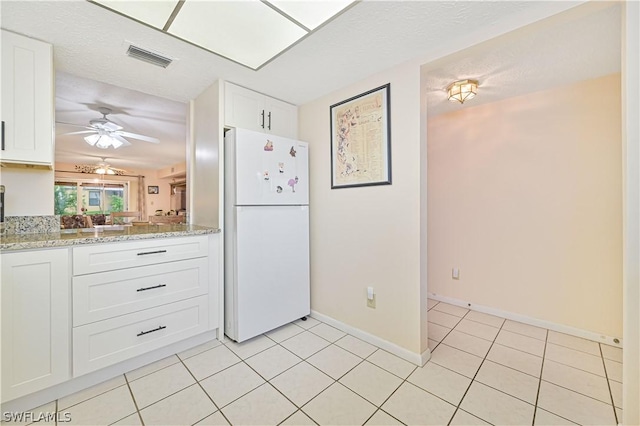 kitchen with light tile patterned flooring, white refrigerator, white cabinetry, and light stone counters