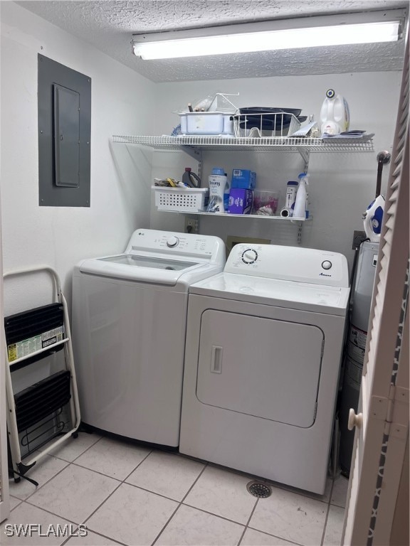 clothes washing area featuring washer and dryer, light tile patterned floors, a textured ceiling, and electric panel