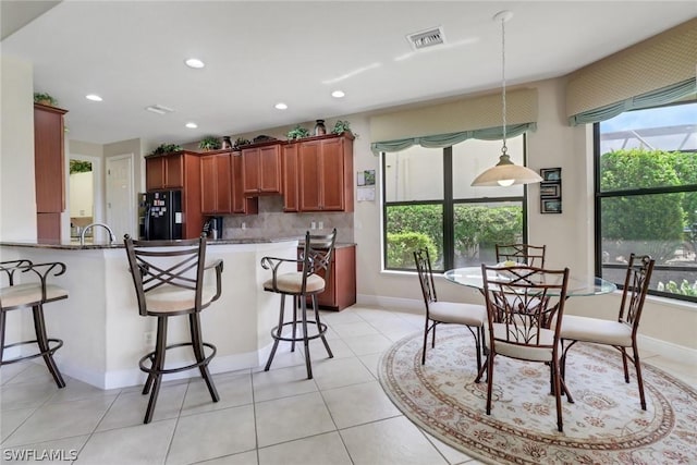 kitchen featuring stone counters, backsplash, a kitchen bar, black fridge with ice dispenser, and kitchen peninsula