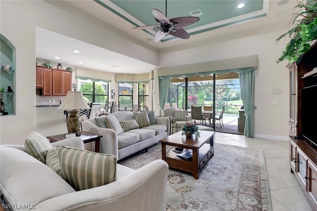 living room with ceiling fan, a tray ceiling, a wealth of natural light, and light tile patterned floors