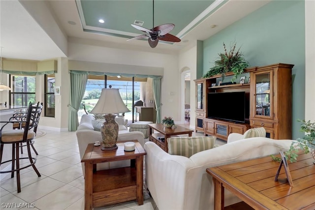 living room featuring light tile patterned floors, plenty of natural light, a raised ceiling, and ceiling fan