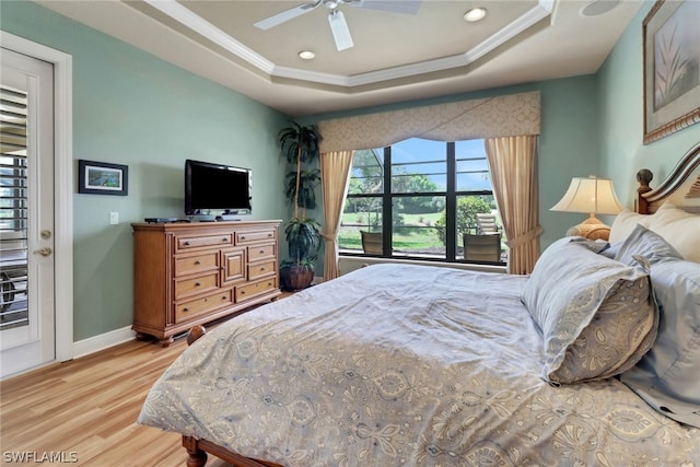 bedroom with crown molding, a tray ceiling, light hardwood / wood-style flooring, and ceiling fan