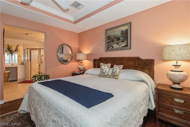 bedroom with hardwood / wood-style flooring, a raised ceiling, ensuite bath, and ceiling fan