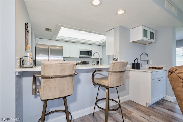 kitchen featuring appliances with stainless steel finishes, a breakfast bar area, white cabinets, and light wood-type flooring