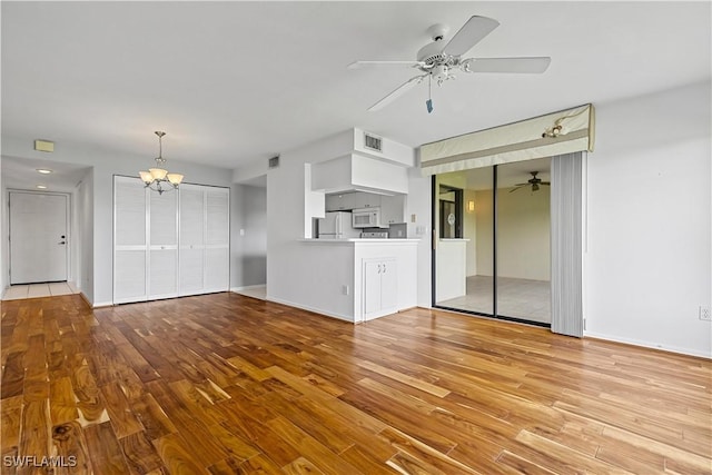 unfurnished living room featuring ceiling fan with notable chandelier and light hardwood / wood-style flooring