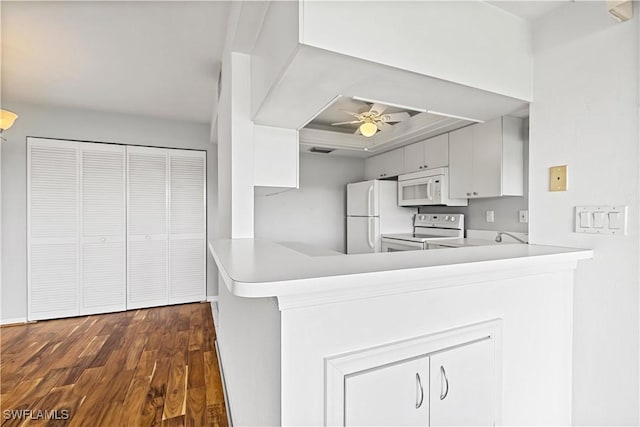 kitchen featuring white appliances, white cabinetry, dark hardwood / wood-style floors, ceiling fan, and kitchen peninsula