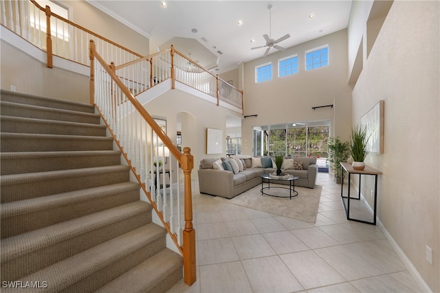 living room featuring light tile patterned floors, ceiling fan, ornamental molding, and a towering ceiling